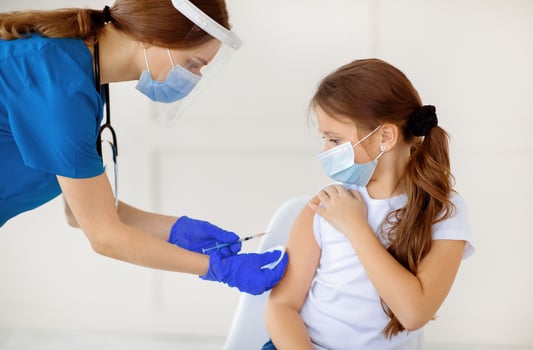 Covid-19 vaccination campaign. Little girl in protective mask receiving coronavirus vaccine injection from doctor at hospital. Antiviral immunization, infectious disease prevention concept photo