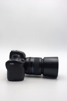 Digital camera with a large lens positioned horizontally on a plain background showcasing its design and features photo