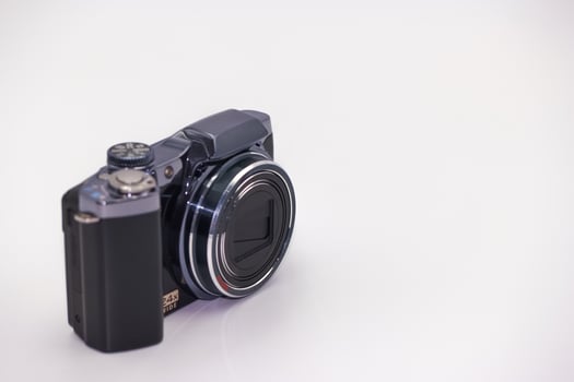 Compact digital camera positioned on a white surface showcasing modern design with clear lens and creative potential photo