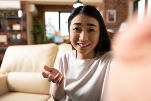 Joyful self employed woman gesturing to camera during home livestream, sharing business insights. Confident asian woman connects with online audience through friendly content. photo