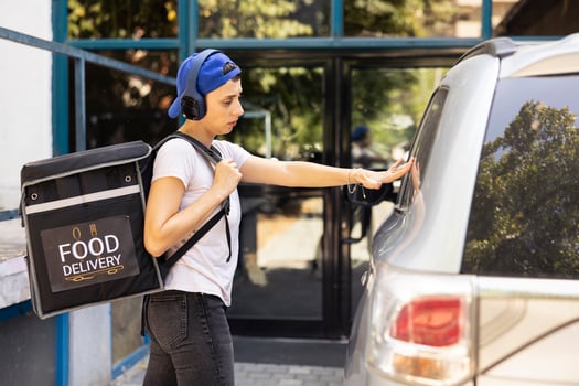 Delivery worker from a restaurant brings food by car to customers, delivering meal in a thermal backpack at the front door. Courier ensuring the order drop off in the driveway, quick service. photo
