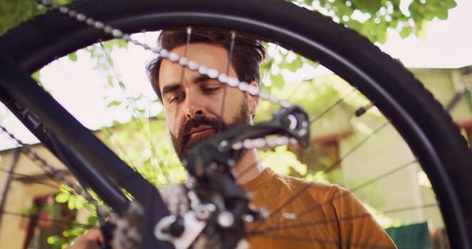 Close-up shot showing bicycle wheel being inspected and repaired by young dedicated caucasian man outdoor. Healthy active man examining bike tire for damages to fix with specialized tool in yard. photo