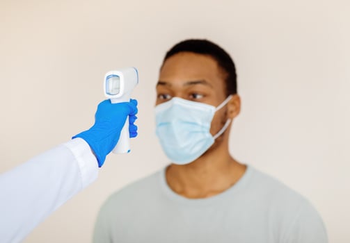 Doctor measuring black man's temperature with electronic thermometer before covid-19 vaccination at clinic. African American guy in medical mask taking part in coronavirus immunization campaign photo