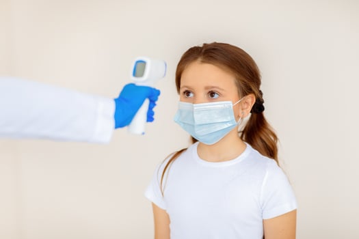 Little girl in face mask having her temperature checked by electronic thermometer while waiting for covid-19 vaccination at hospital. Coronavirus immunization campaign concept photo