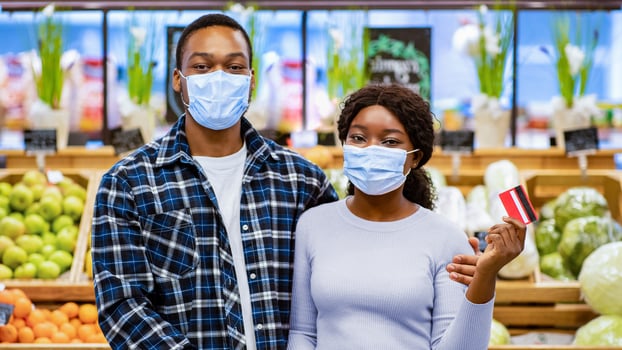 Portrait of black couple wearing protective masks and holding credit card at shopping mall during coronavirus pandemic. Millennial African American guy and lady recommending contactless payment photo