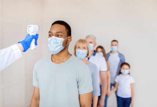 Coronavirus immunization medical campaign concept. Black man in face mask standing in line at clinic, doctor measuring his temperature with infrared thermometer before covid-19 vaccination, copy space photo