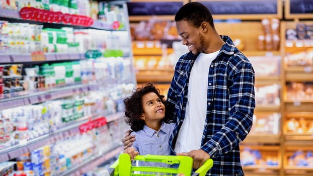 Happy black dad and his pretty little daughter with shopping trolley having great time buying groceries at big mall. African American parent with kid purchasing foodstaff at hypermarket photo