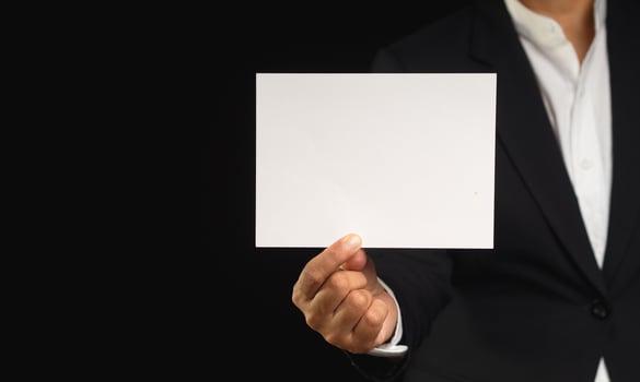 Businessman in a black suit holding a blank white paper while standing on a black background photo