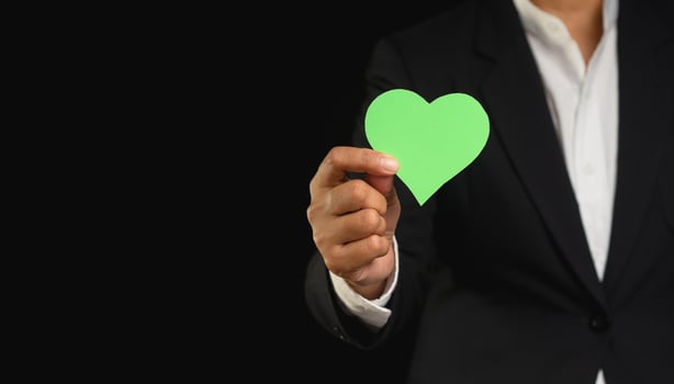 Close-up of a hand holding a green heart shape symbol while standing against a black background. photo