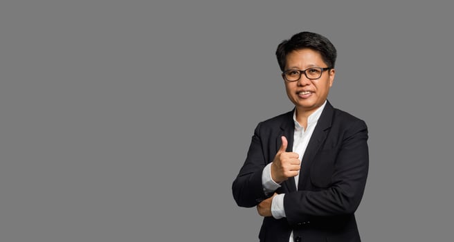 Portrait of a businesswoman with short black hair hand showing thumbs up while standing on a gray background. photo