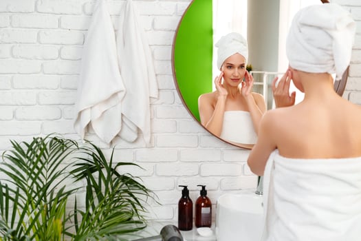 Woman applies skincare in a bright bathroom with plants and a mirror during morning routine photo