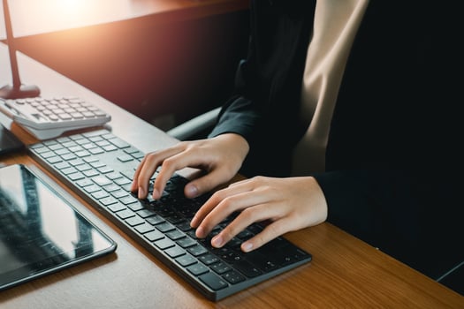 Close-up of hands typing on a keyboard in a modern office environment with sunlight streaming in. photo