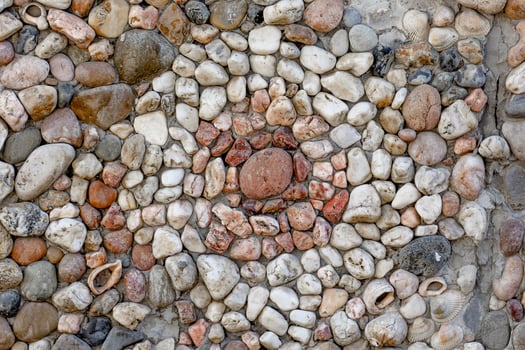 A detailed close-up of a decorative pebble mosaic featuring a central circular design made of smooth, multicolored stones and scattered seashells photo