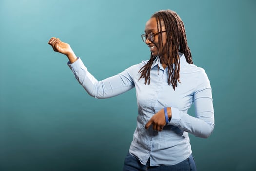 Smiling black woman with glasses having a good time in blue background studio. African american female individual standing and playing an imaginary guitar, feeling happy and optimistic for new day. photo