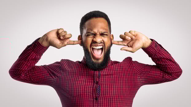 Mad Black Man Shouting Covering Ears With Hands And Closing Eyes Posing Over White Background In Studio. Negative Emotion, Madness And Stress. Too Loud Concept photo