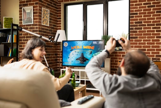 White man and woman relax together, celebrating shared game victory. Young caucsasian adults with raised hands, cheering and enjoying drinks on sofa while TV flashes winning message. photo