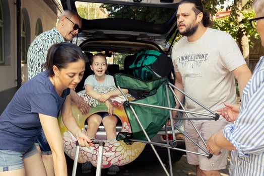 Grandparents help their son and daughter in law load the car trunk while a little girl watches with joy, big group excited about family getaway to the seaside. Relaxing road trip lifestyle. photo
