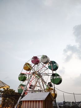 A mini Ferris wheel with a sunset sky in the background. The gondolas, or cabins, of the Ferris wheel are brightly colored. An amusement ride on the rooftop of a shopping center. copy space. photo