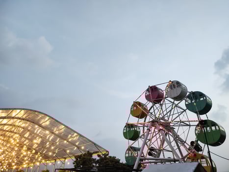 A mini Ferris wheel with a sunset sky in the background. The gondolas, or cabins, of the Ferris wheel are brightly colored. An amusement ride on the rooftop of a shopping center. Negative space. photo
