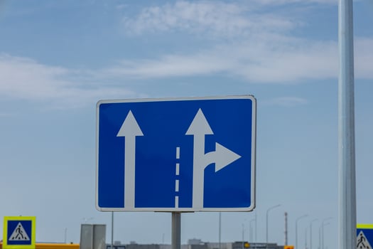 Road sign displays directions for vehicles traveling straight or turning right at a busy urban intersection during the day photo