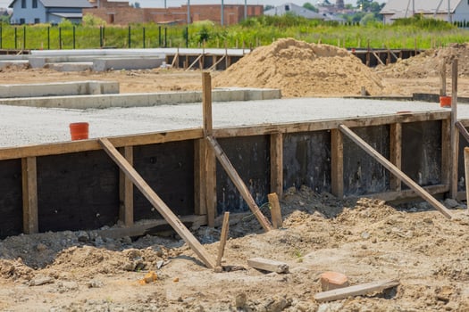 Workers are preparing a concrete foundation for a new residential building, with wooden supports installed and sandy terrain surrounding the area photo