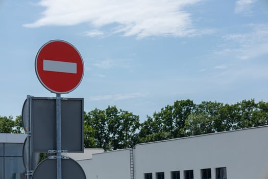 A prominent no entry sign is visibly placed outside a contemporary building under a bright blue sky with scattered clouds photo