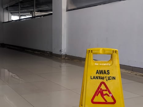 Bright yellow safety sign displaying AWAS LANTAI LICIN and a falling person icon, positioned on a reflective tiled floor, alerting to a wet and hazardous surface in Banjarsari, West Java. photo