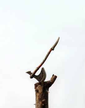 Tiny ancient ax firmly planted in a wooden stump. Ax blade is made of dark metal, with curved handle. Texture of wood and metal is clearly visible. photo