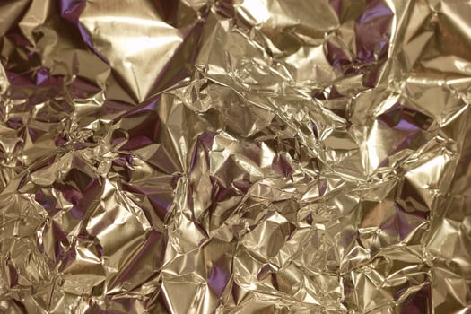Shiny crumpled metallic foil in various shades reflecting light and creating interesting textures in a close up view photo