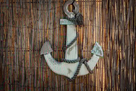 Rustic anchor adorned with frayed rope against a woven backdrop creates an inviting coastal atmosphere in this charming nautical decor photo