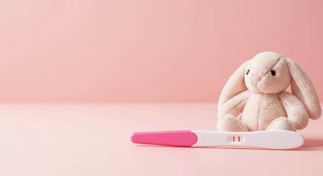 Positive pregnancy test with a cute bunny toy on pink. photo