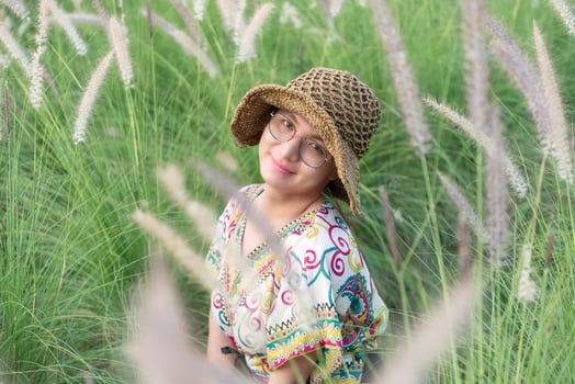 A girl in a hat and glasses sitting in tall grass photo