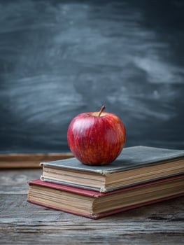 Desk With Apple and Stacked Books Beside Chalkboard in Classroom Setting photo