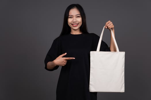 Front View of Woman Holding Blank Canvas Tote Bag, Eco-Friendly Reusable Fabric with Handle, Close-Up Mockup, No Plastic and Environmental Smiling Concept photo