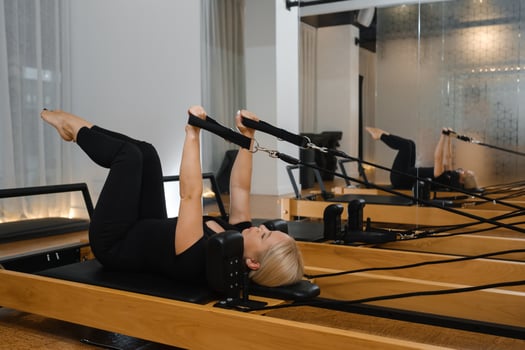 Woman practicing Pilates on reformer equipment in a bright studio with mirrors during a morning session focused on strength and flexibility exercises photo