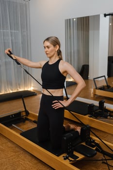 Fitness enthusiast performing a pilates workout on a reformer in a modern studio during a morning class photo