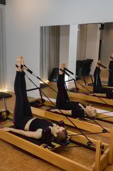Pilates session showcasing two individuals performing leg exercises on reformers in a modern fitness studio photo
