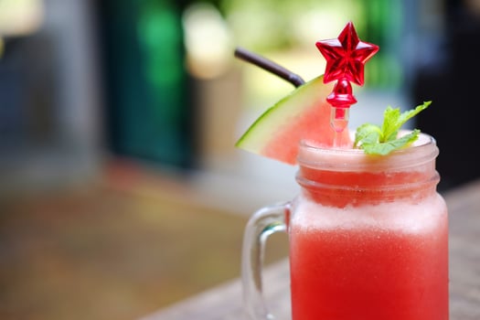 Close up a glass of watermelon smoothie with red star spoon on wooden table in cafe. Copy space photo