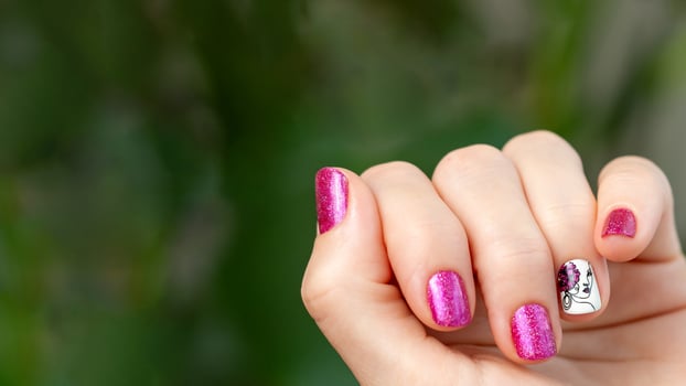 Female hand with pink manicure. Woman fingernails with pink holographic nail polish lacquer on green lush background. Aesthetic visual of red violet manicure with lady silhouette stamping. Copy space photo