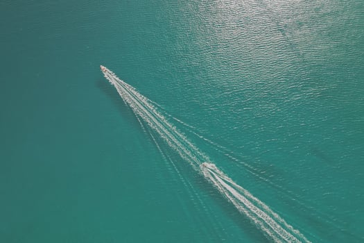Two boats are sailing one after another across crystal clear sea water, aerial drone photo with white trails behind