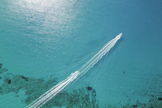 Two small boats sailing one after another across crystal clear sea water, aerial drone photo with white trails behind
