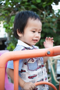 Little boy smiling while playing with a toy climbing at the playground on a sunny day. Kid enjoying springtime or summer outdoors and climbing. Asian child aged 2 years old. Vertical image. photo