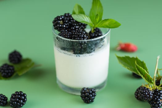 Ripe blackberries with homemade yogurt in a glass on a green background photo