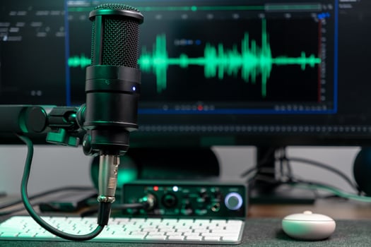 Black studio microphone with glowing green audio wave visualizer on computer monitor, representing professional podcasting, voice recording, and sound engineering photo