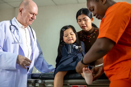 Little asian girl having accident with ankle sprain gets treatment from nurse and senior doctor in the hospital emergency unit with elastic bandage for healthcare and kid insurance concept photo