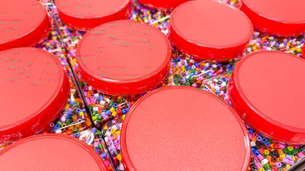 Rows of vibrant red lidded containers cradle multicolored beads spark creativity, artisan charm, Pi Day celebrations, or DIY crafts photo