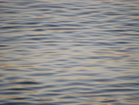 A tranquil close-up of gently rippling water illuminated by warm, golden light from a sunset. Wave pattern for wellness, nature, or background theme concepts photo