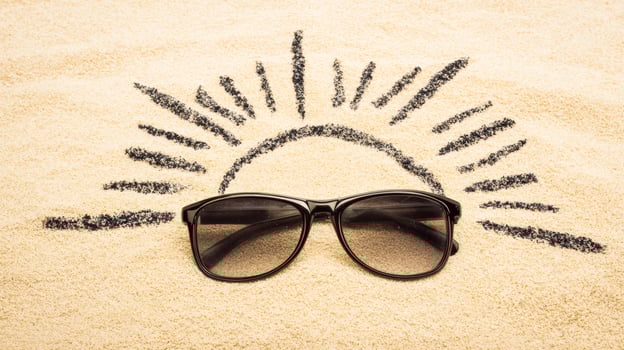 Sunglasses on sand with sun. Sunglasses are placed on sand, surrounded by a drawn sunburst, suggesting a beach setting in bright daylight. photo
