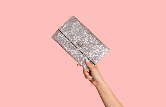 Young woman showing silver sparkly clutch bag on pink background, closeup of hand photo