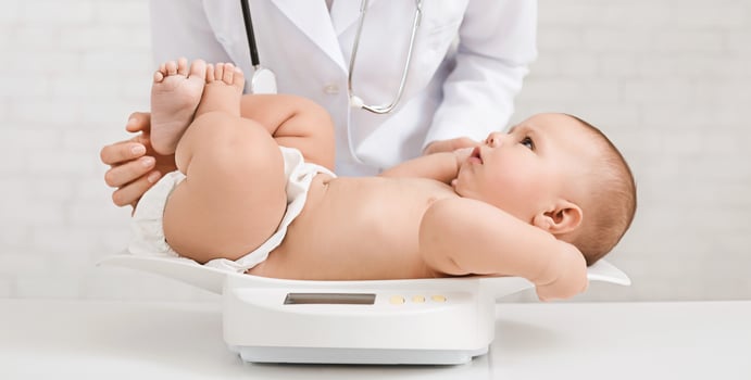 Female doctor weighing cute baby in clinic, measuring weight on scales, panorama photo